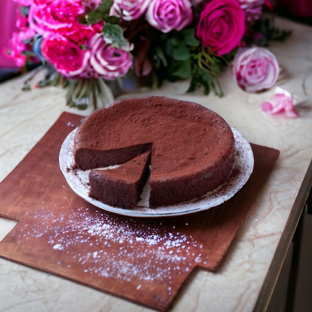 Close up image of our Chocolate Jalapeno Cake dusted with cocoa powder on a plate, placed on a cutting board with a bunch of flowers on the side of the table